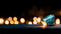 Raw blue apatite crystal on dark wooden surface with warm glowing bokeh lights creating magical atmospheric backdrop for spiritual and wellness designs.