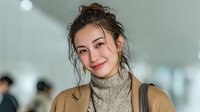 Young Asian woman with messy bun hairstyle wearing beige turtleneck sweater smiling warmly in modern office environment for lifestyle and business content.