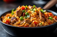 Homemade chicken and vegetable fried rice in black bowl, garnished with green onions and sesame seeds, close-up view on dark background with selective focus.