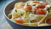Creamy fettuccine pasta with smoked salmon pieces and fresh dill garnish in ceramic bowl, selective focus on tender fish and herbs against blurred background.