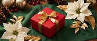 Red gift box with golden ribbon surrounded by white poinsettias, pine cones and Christmas ornaments on green fabric background for holiday celebrations.