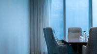 Modern office conference room with empty chairs at wooden table, floor-to-ceiling windows, and sheer curtains filtering natural light for corporate meetings.