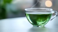 Steaming glass cup of fresh green tea on white surface with soft bokeh background and vapor rising, creating tranquil morning atmosphere.