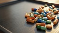 Colorful pharmaceutical pills and capsules scattered on dark wooden surface for medical healthcare and medication concepts.