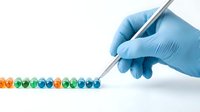 Gloved hand using tweezers to arrange colorful capsules in a row on white background, representing pharmaceutical research and drug development.