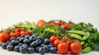 Fresh organic vegetables and blueberries arranged on white background featuring broccoli, cherry tomatoes, peas and herbs for healthy eating and nutrition.