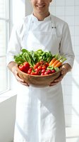 Chef in white apron holding wooden bowl of fresh vegetables including tomatoes, lettuce, carrots and peppers in bright kitchen for culinary and food service use.