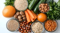 Fresh healthy ingredients with nuts, grains, vegetables, and citrus fruits arranged on white background. Clean eating and balanced nutrition concept.