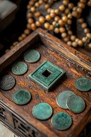 Ancient Chinese copper coins with patina and square hole arranged on vintage wooden box with pearl necklace, showing traditional currency artifacts.