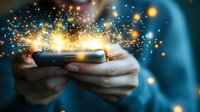 Magical glowing sparkles burst from smartphone screen held in hands against dark background, creating ethereal light effect with bokeh and particles.