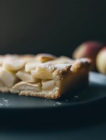 Fresh homemade apple pie slice with layered fruit filling on dark plate, moody lighting and selective focus creates rustic atmosphere for food photography.