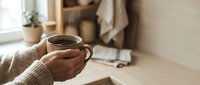 Hands holding warm coffee mug in cozy home interior with soft natural lighting creating peaceful morning atmosphere for relaxation and comfort.