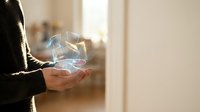 Close-up of hands holding glowing digital hologram with light particles and data visualization in modern office environment.