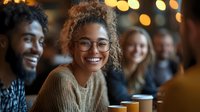 Young diverse friends enjoying coffee together at cafe with warm lighting and bokeh background, sharing genuine laughter and conversation during casual meetup.