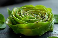 Fresh green avocado rose garnished with black sesame seeds on dark slate background, macro food photography for restaurant menu and culinary blogs.