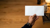 Male hand holding blank white card on wooden surface with warm lighting for business, marketing, or promotional use.