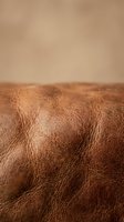 Close-up macro view of brown leather texture with natural grain patterns and wrinkles showing craftsmanship detail for luxury goods and fashion design.