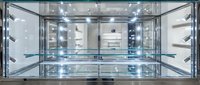 Modern glass display cabinet with chrome frame and illuminated shelves, open front view, retail showcase for jewelry or luxury goods.