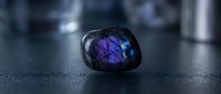 Purple and blue labradorite gemstone with iridescent flash on dark surface showcasing natural mineral beauty and mystical properties for jewelry design.