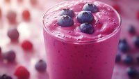 Fresh blueberry smoothie with whole berries on top in glass, healthy breakfast drink with vibrant purple color for nutrition and wellness content.