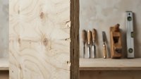 Wooden plywood panel with visible grain and knots in carpentry workshop with traditional woodworking tools on shelf in background for construction projects.