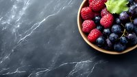Fresh mixed berries in wooden bowl on dark marble surface with copy space for healthy eating and nutrition concepts.