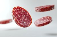 Flying sliced salami sausage pieces on light background with soft shadows. Levitating meat product in modern food photography style.