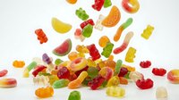 Colorful gummy bears and fruit candies scattered on white background. Sweet treats for confectionery, dessert concepts and candy shop promotions.