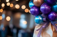 Festive purple and blue shiny balloons with sparkly ribbon decoration against blurred bokeh lights background, creating magical party atmosphere.