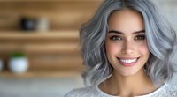 Young woman with trendy silver gray wavy hair and bright smile wearing white sweater against blurred modern interior background. For beauty and fashion blogs.