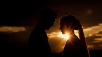 Romantic couple silhouettes sharing intimate moment at golden sunset with dramatic sky. Wedding photography concept for love and relationship themes.