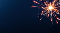 Glowing orange sparkler against dark blue background creates dramatic light trails and bursts, capturing festive celebration moment with dynamic energy.