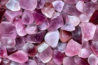 Collection of polished amethyst gemstone chips in various purple and pink hues creating natural crystal healing stone background texture for jewelry making.