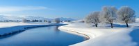 Serene winter landscape with snow-covered riverbank and bare trees under blue sky. Peaceful frozen water scene perfect for seasonal marketing materials.
