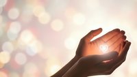 Cupped hands holding glowing heart symbol with warm bokeh lights background representing love, care, compassion, charity, hope, protection and emotional wellness.