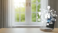 Smart home technology concept with digital icons floating above smartphone on wooden desk near bright window for modern living automation solutions.