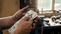 Elderly craftsman hands shaping clay in pottery workshop with natural lighting and traditional tools creating handmade ceramic art piece.