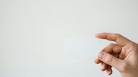 Adult hand holding blank white card against neutral background, suitable for business branding, marketing mockups, and promotional material presentations.