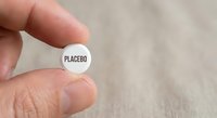 Hand holding white placebo pill tablet between fingers on neutral background for medical research and pharmaceutical studies.