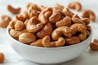 Roasted cashew nuts in white ceramic bowl on light background, close up view of healthy organic snack, natural protein source for vegetarian diet.