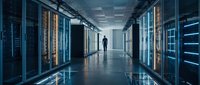 Modern data center corridor with server racks and silhouette of IT professional walking through illuminated technology infrastructure for business computing.