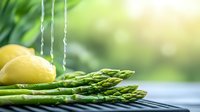 Fresh green asparagus spears with water drops and lemon on blurred natural background. Raw organic vegetables for healthy cooking concept.