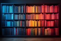 Bookshelf with color-coordinated books arranged in spectrum from cool blue to warm red tones creating dramatic ombre effect against dark background. Perfect for education themes.