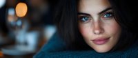 Young woman with striking blue eyes, freckles and dark hair gazes intensely at camera. Dramatic bokeh lighting creates moody atmospheric portrait with shallow depth of field.