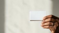 Hand holding blank white card against neutral background, suitable for business branding, marketing mockups, and corporate identity design projects.