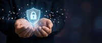 Businessman holding glowing digital shield with padlock icon, symbolizing cybersecurity, data protection, and network safety in dark blue background.