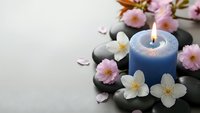 Zen spa composition with blue candle, smooth stones and delicate pink flowers on neutral background for relaxation and wellness concepts.