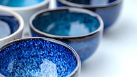 Handcrafted ceramic bowls with deep blue crystalline glaze finish arranged in minimalist composition, showcasing artisanal pottery craftsmanship and organic textures.