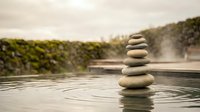Zen stone stack balanced on calm water surface creating ripples with natural landscape background for meditation and wellness concepts.
