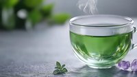 Steaming green tea in transparent glass cup with fresh mint leaves and purple crystals on gray background. Calming wellness composition.